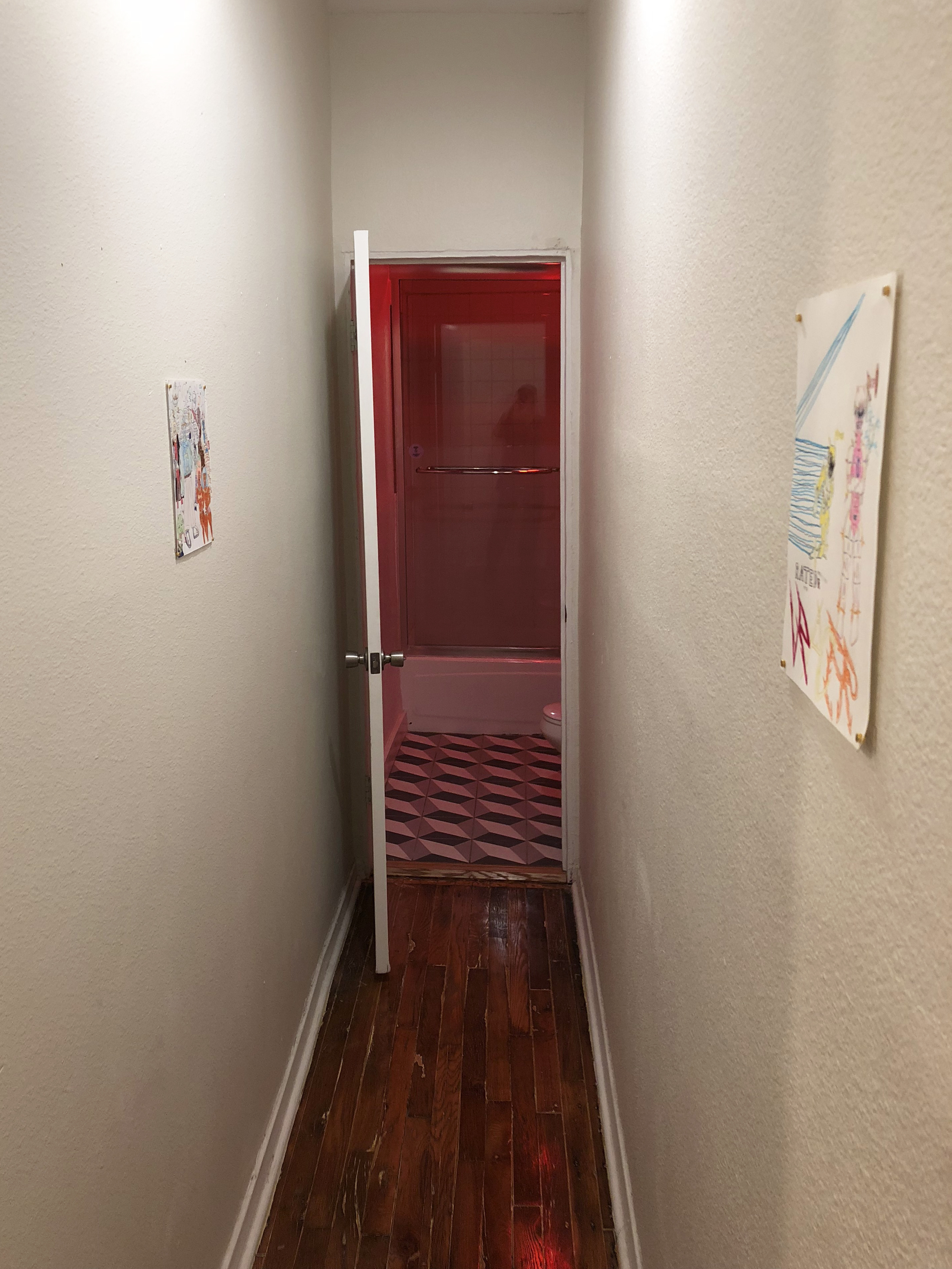 Two drawings hung in a narrow hallway leading to a bathroom with red lighting in it